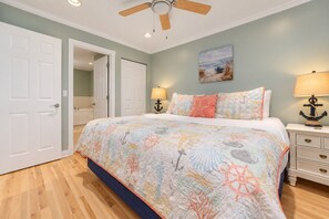 A bedroom with a bed, two bedside lamps, a ceiling fan, and a painting on the wall. - Bay Breeze 107 | Beachfront Condo | Near Downtown & Tart Trail (Traverse City)