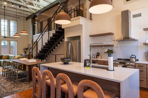 A modern kitchen with a central island, stainless steel appliances, and a staircase leading to an upper level. - The Miss Lou (New Orleans)