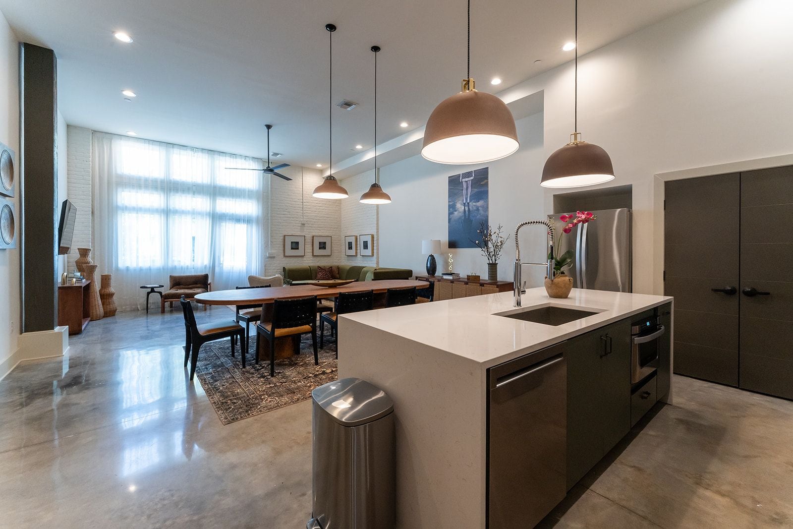 A modern kitchen with a central island, pendant lighting, and a dining area with a sofa and chairs.