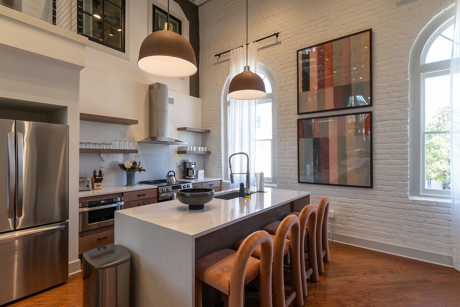 A modern kitchen with a central island, stainless steel appliances, pendant lighting, and a large window.