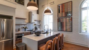 A modern kitchen with a central island, stainless steel appliances, pendant lighting, and a large window.