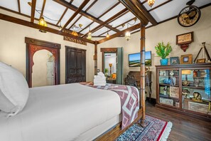 Ein Schlafzimmer mit einem großen Bett, Holzbalkendecke, einem Spiegel, einem Kleiderschrank und einer Kommode mit Dekoration.