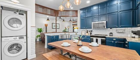 A modern kitchen with blue cabinets, a wooden dining table, and a built-in washing machine.