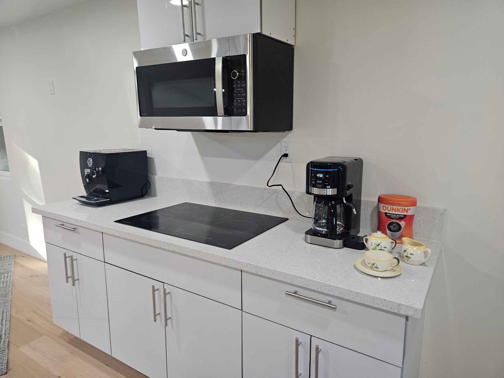 Een moderne keuken met een magnetron, koffiezetapparaat en een DUNKIN' N' DONUTS beker.
