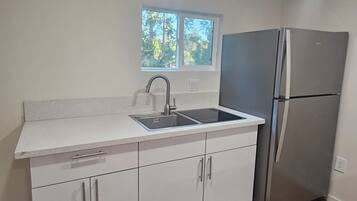 A kitchen with a stainless steel refrigerator, a double sink, and white cabinetry.
