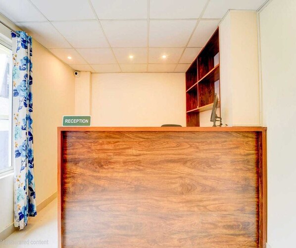 Ein Empfangsschalter mit einem Schild, ein Fenster mit Vorhängen und ein Holzregal.