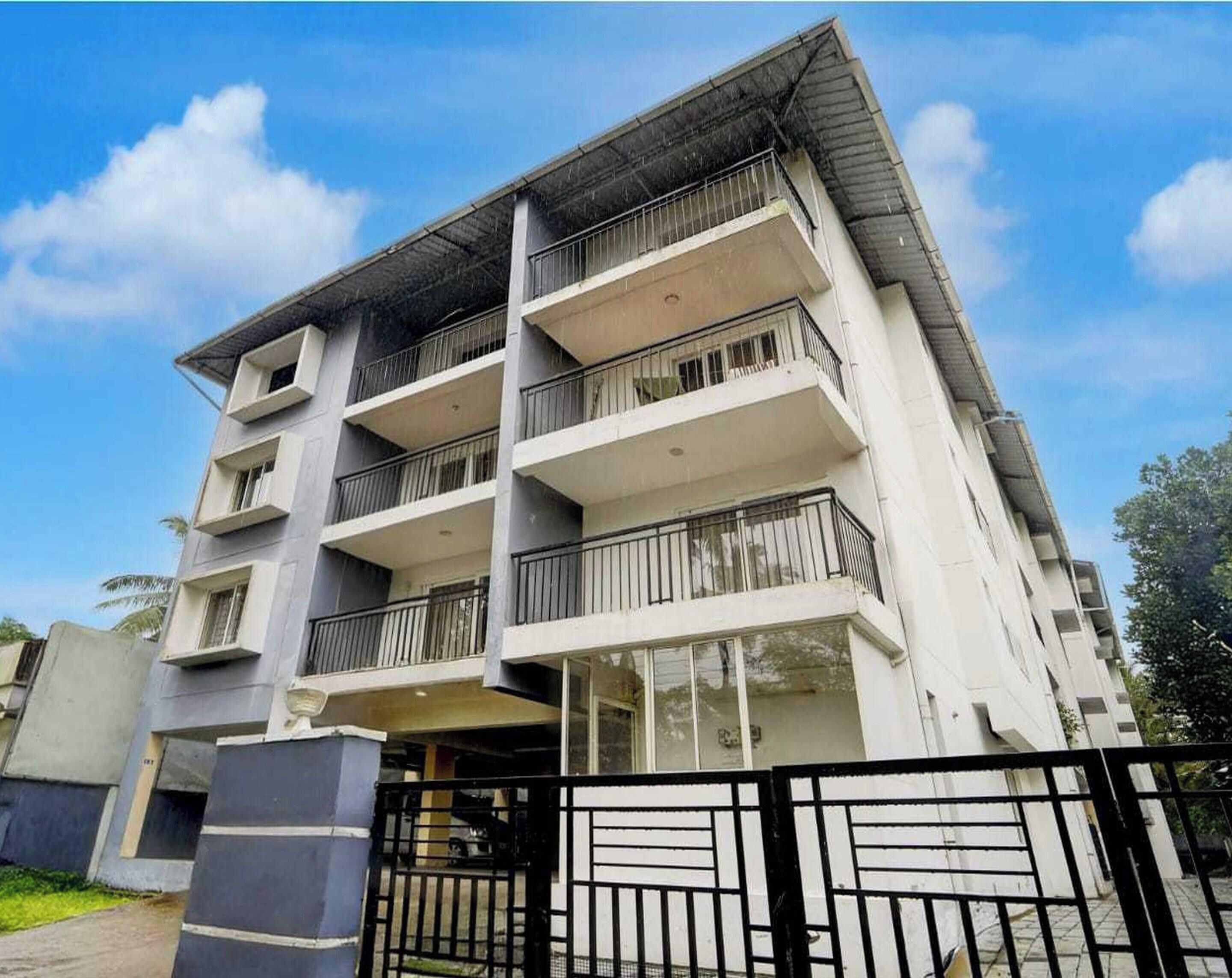 A multi-story residential building with balconies, a gated entrance, and a clear sky.