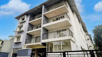 A multi-story residential building with balconies, a gated entrance, and a clear sky.