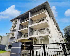 A multi-story residential building with balconies, a gated entrance, and a clear sky. - Classic Periyar Stay (Peermade)