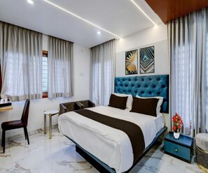 A modern hotel room with a large bed, a desk, and a chair. There are two artworks on the wall, a window with curtains, and a vase with flowers on the nightstand. - Classic Periyar Stay (Peermade)