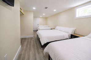 A hotel room with three beds, a flat-screen TV mounted on the wall, and a window providing natural light. - 8-Beds Big Stay, 10Mins NYC, Free Reserved Parking (Jersey City)