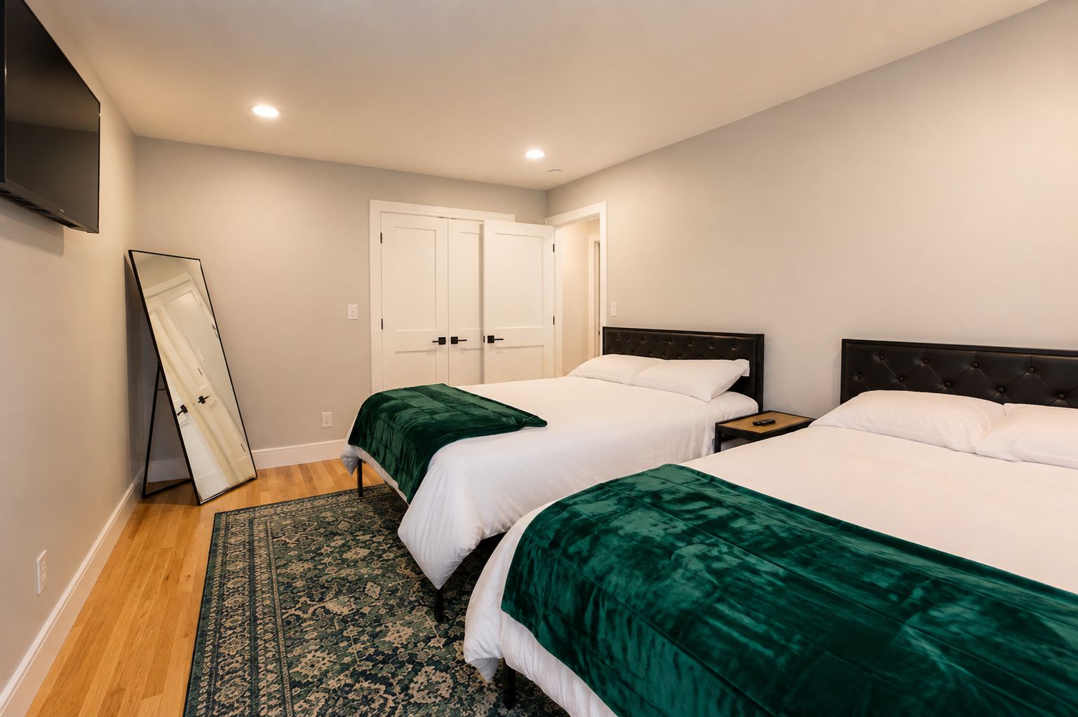 A hotel room with two beds, a large mirror, a flat-screen TV, and a patterned rug.