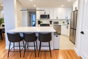 A modern kitchen with white cabinets, stainless steel appliances, and a central island with bar stools. - 8-Beds Big Stay, 10Mins NYC, Free Reserved Parking (Jersey City)