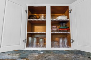 A cabinet with two shelves, one containing glassware and the other with storage containers.