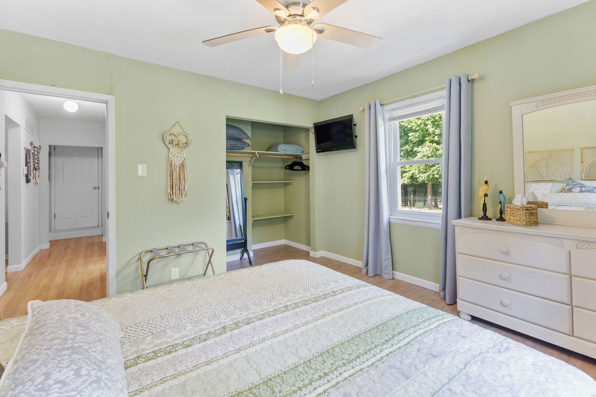 A bedroom with a bed, a dresser, a closet, a ceiling fan, and a window with curtains.