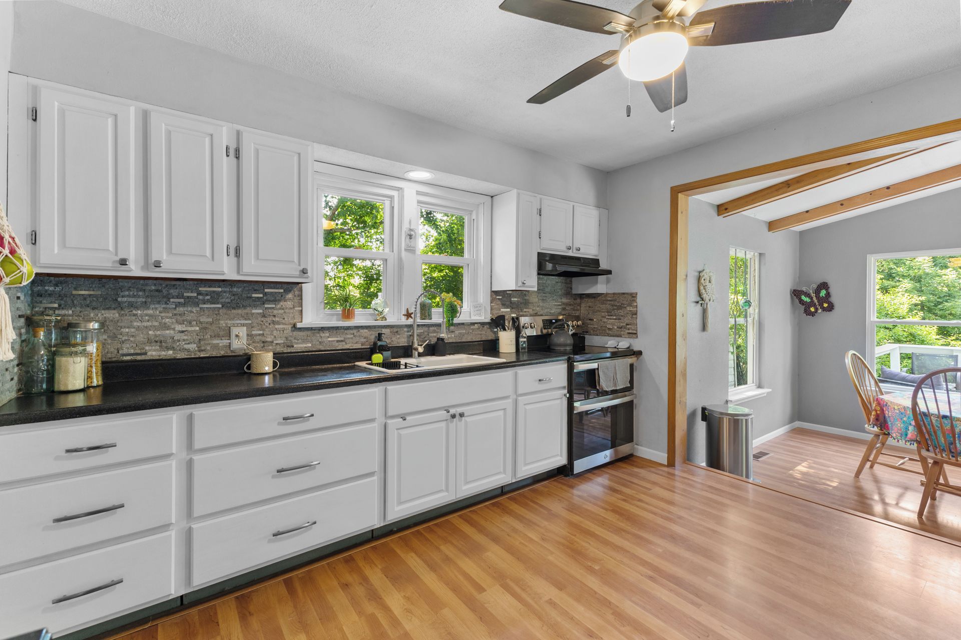A modern kitchen with white cabinets, a black countertop, and a wooden floor.