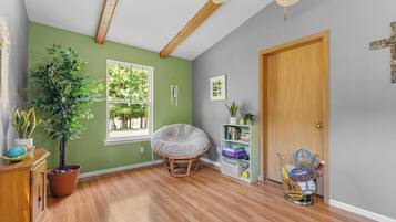 A room with a wooden floor, a green wall, a window, a door, and a bookshelf with books and a plant.