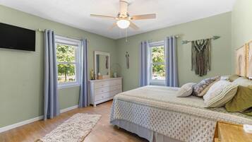 A bedroom with a bed, dresser, mirror, ceiling fan, windows, and a rug.