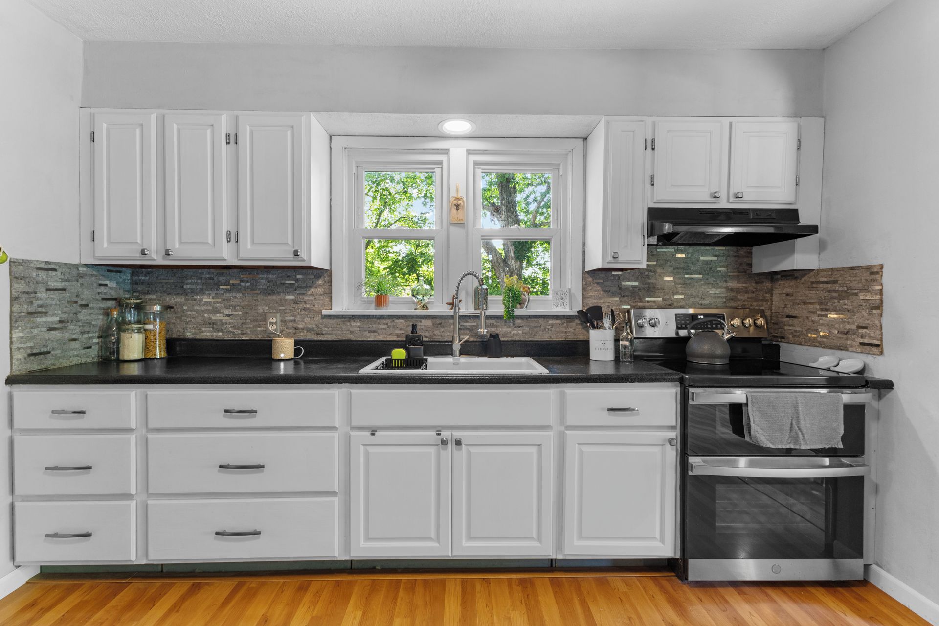 A modern kitchen with white cabinetry, a black countertop, and a stainless steel oven.