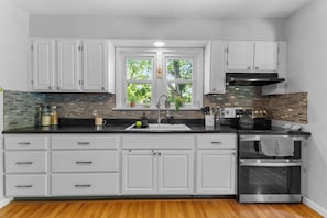 A modern kitchen with white cabinetry, a black countertop, and a stainless steel oven.