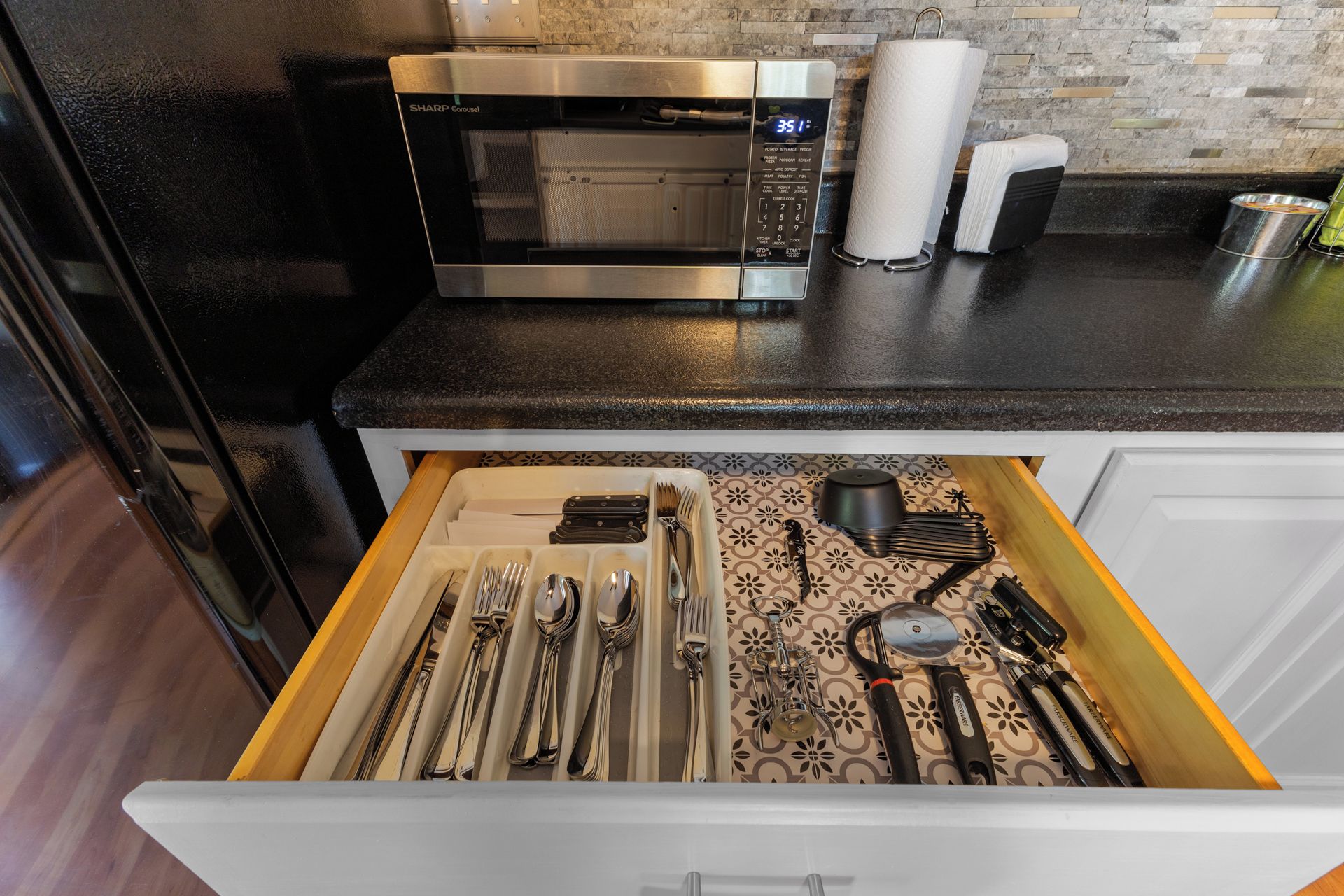 Een keuken met een magnetron, een papieren handdoekdispenser en een lade met keukengerei.