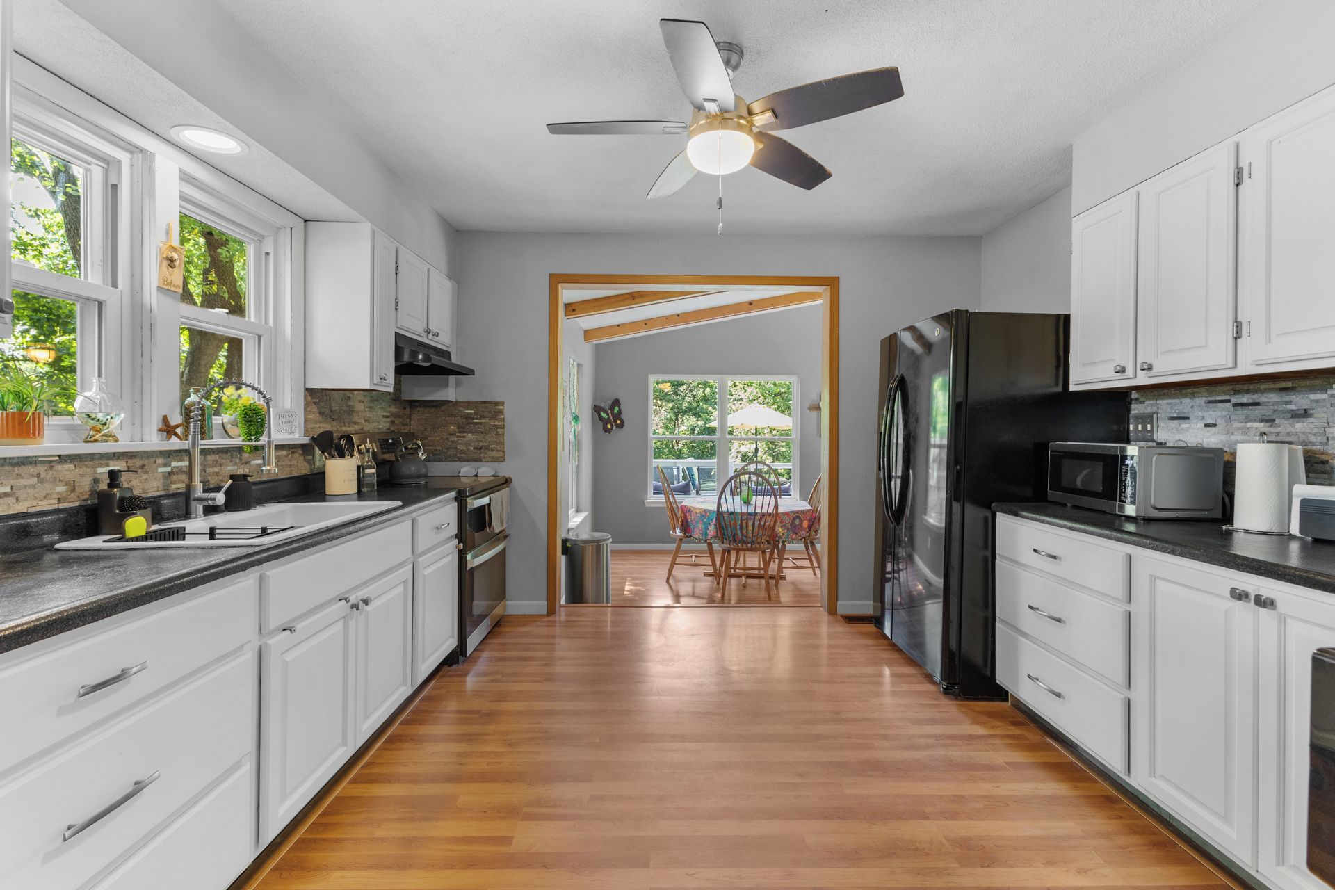 A kitchen with white cabinets, a black refrigerator, and a wooden floor.
