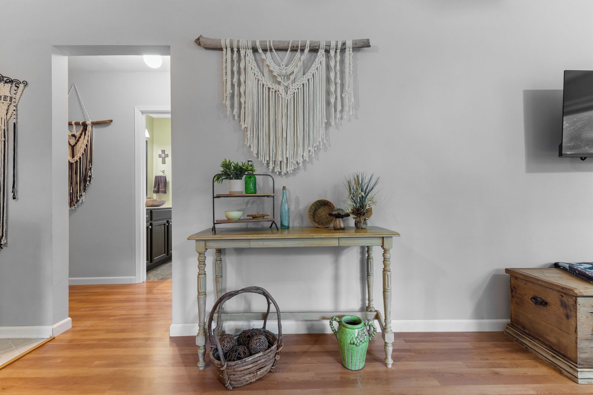 A room with a wooden table, a macrame wall hanging, and a green vase.