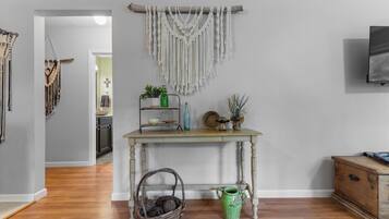 A room with a wooden table, a macrame wall hanging, and a green vase.