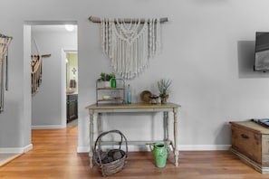 A room with a wooden table, a macrame wall hanging, and a green vase.