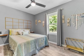 Une chambre à coucher avec un lit, un ventilateur de plafond, une fenêtre avec des rideaux et des éléments de décoration murale.