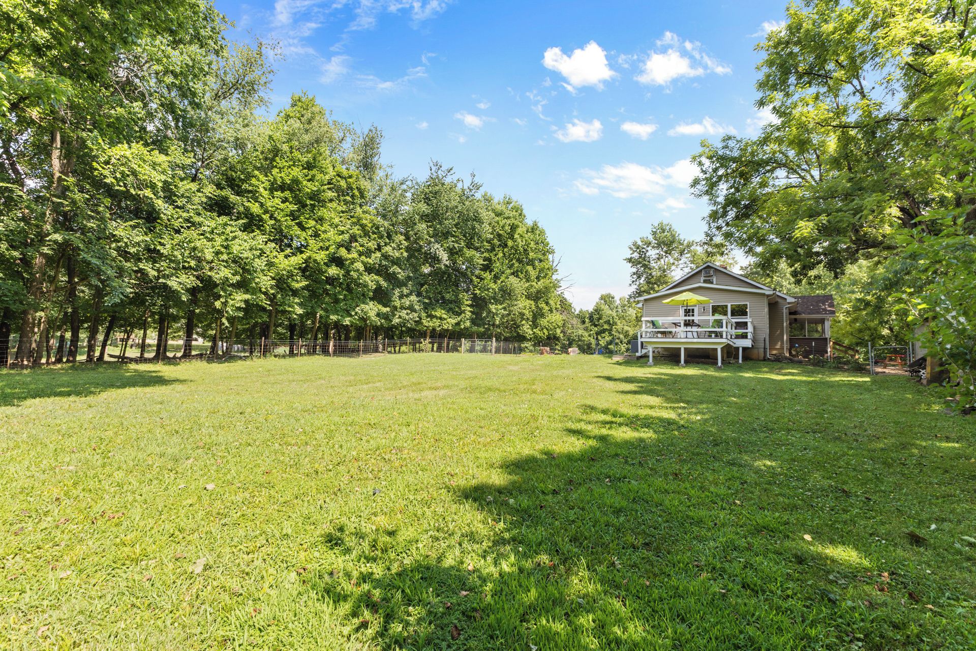 A spacious grassy yard with a house featuring a porch and outdoor seating.