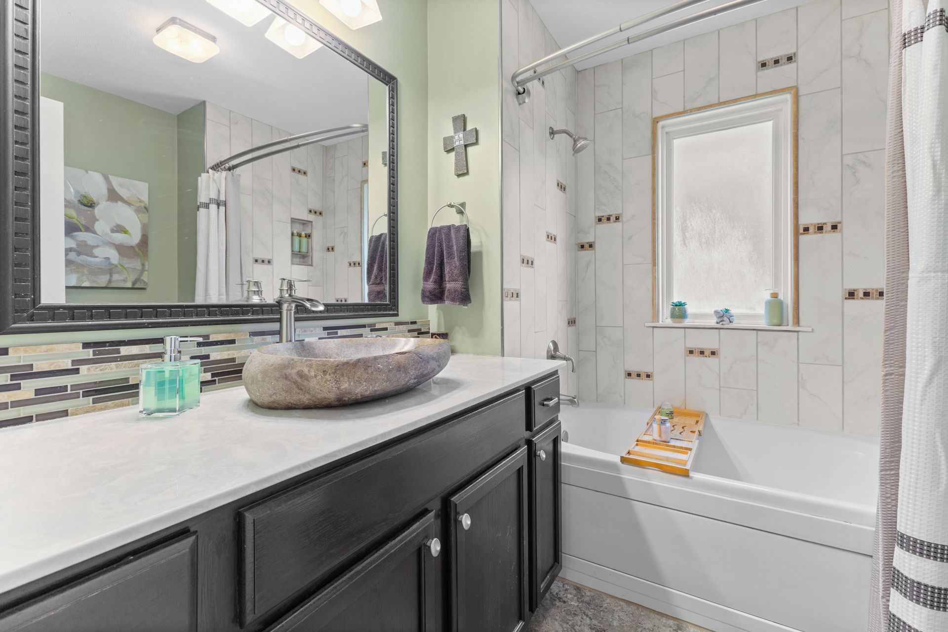 A bathroom with a stone sink, a large mirror, a shower with a glass door, and a window with a view.
