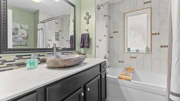 A bathroom with a stone sink, a large mirror, a shower with a glass door, and a window with a view.