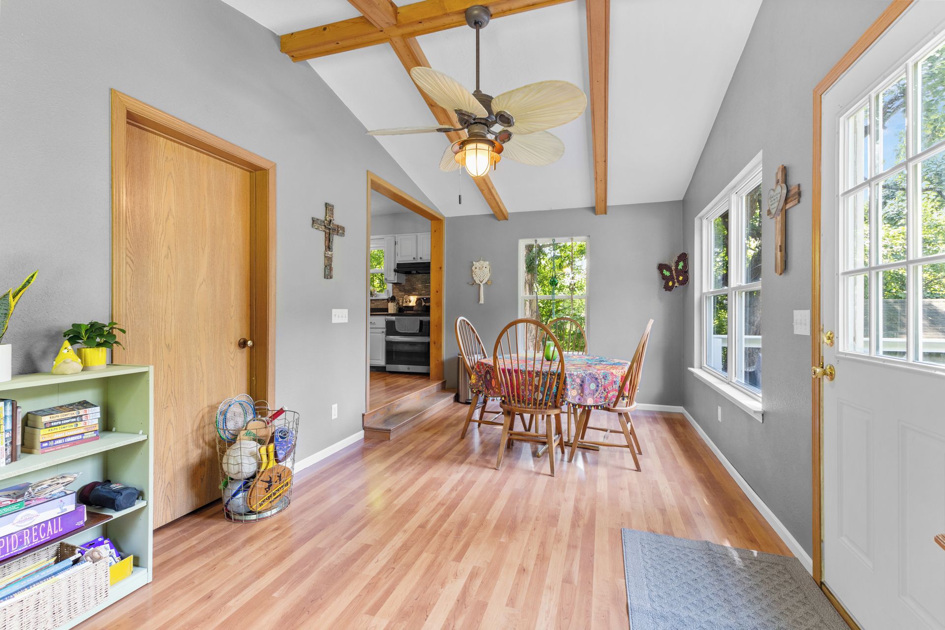 A hallway with wooden flooring, a dining area with a table and chairs, a ceiling fan, and a bookshelf with books and sports equipment.
