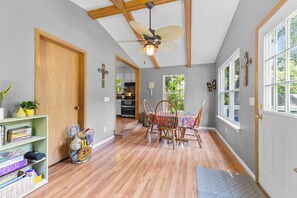 A hallway with wooden flooring, a dining area with a table and chairs, a ceiling fan, and a bookshelf with books and sports equipment.