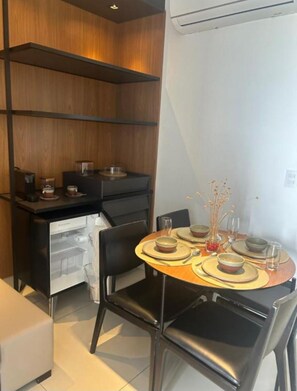 A compact dining area with a round table set for two, a black sofa, and a built-in kitchen unit with shelves. - Apartment in Muro Alto Beach Resort (Ipojuca)