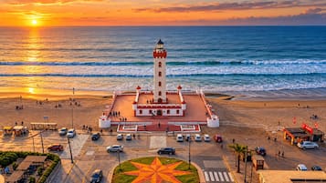 Un faro con fachada roja y blanca, ubicado en una playa con vista despejada al océano.