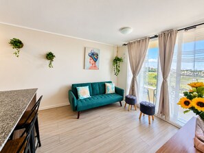 Ein modernes Wohnzimmer mit einem türkisblauen Sofa, einem Esstisch und Blick auf die Stadt.