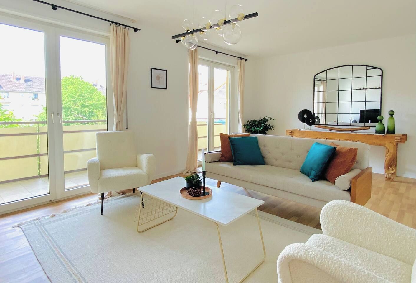 En moderne stue med sofa, lænestole, sofabord og et stort vindue med gardiner.