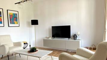 A modern living room with a flat-screen TV, white furniture, and abstract art on the wall.
