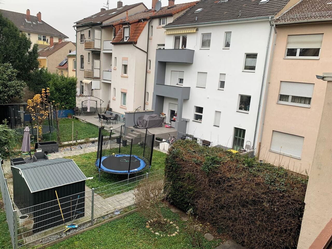 Un quartier résidentiel avec un trampoline installé dans une cour clôturée, entouré d’immeubles à plusieurs étages.