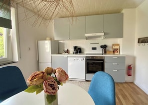 A modern kitchen with white cabinets, a dishwasher, an oven, and a coffee maker. There is a vase with flowers on the table.