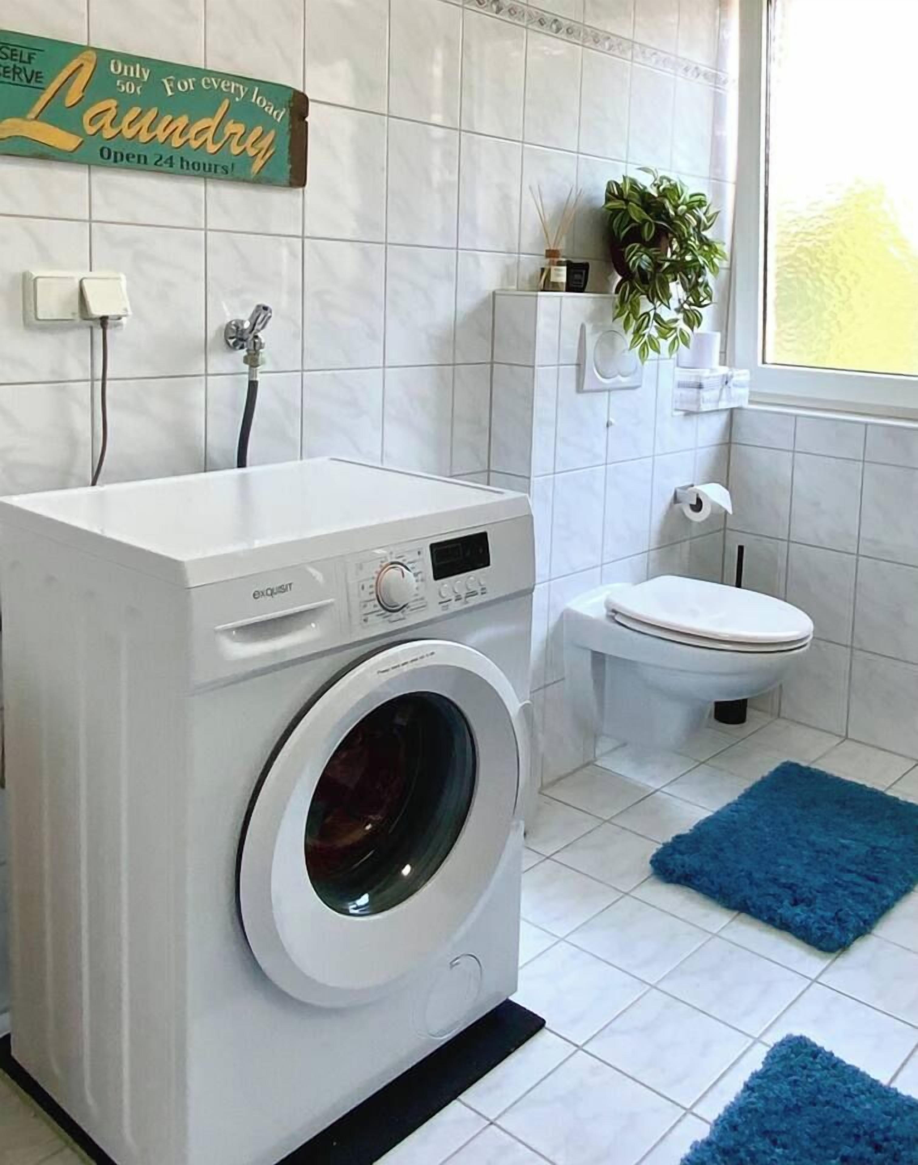 Ein kleiner Waschbereich mit Waschmaschine, Toilette und einem blauen Teppich.