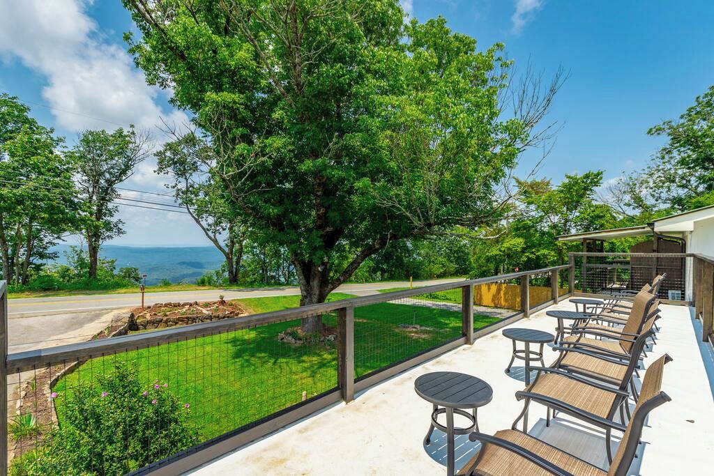 A balcony with outdoor furniture, a view of a tree, and a road in the background.