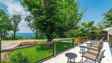 A balcony with outdoor furniture, a view of a tree, and a road in the background.