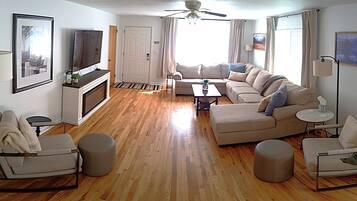 A living room with a fireplace, sofa set, coffee table, and ottomans.