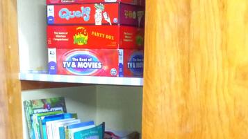 A wooden cabinet with shelves containing various items including books, a board game, and storage bins.