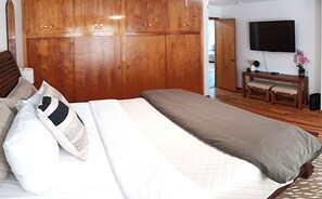 Una camera da letto con un letto, un'armadietto in legno, un comodino e una televisione appesa al muro.