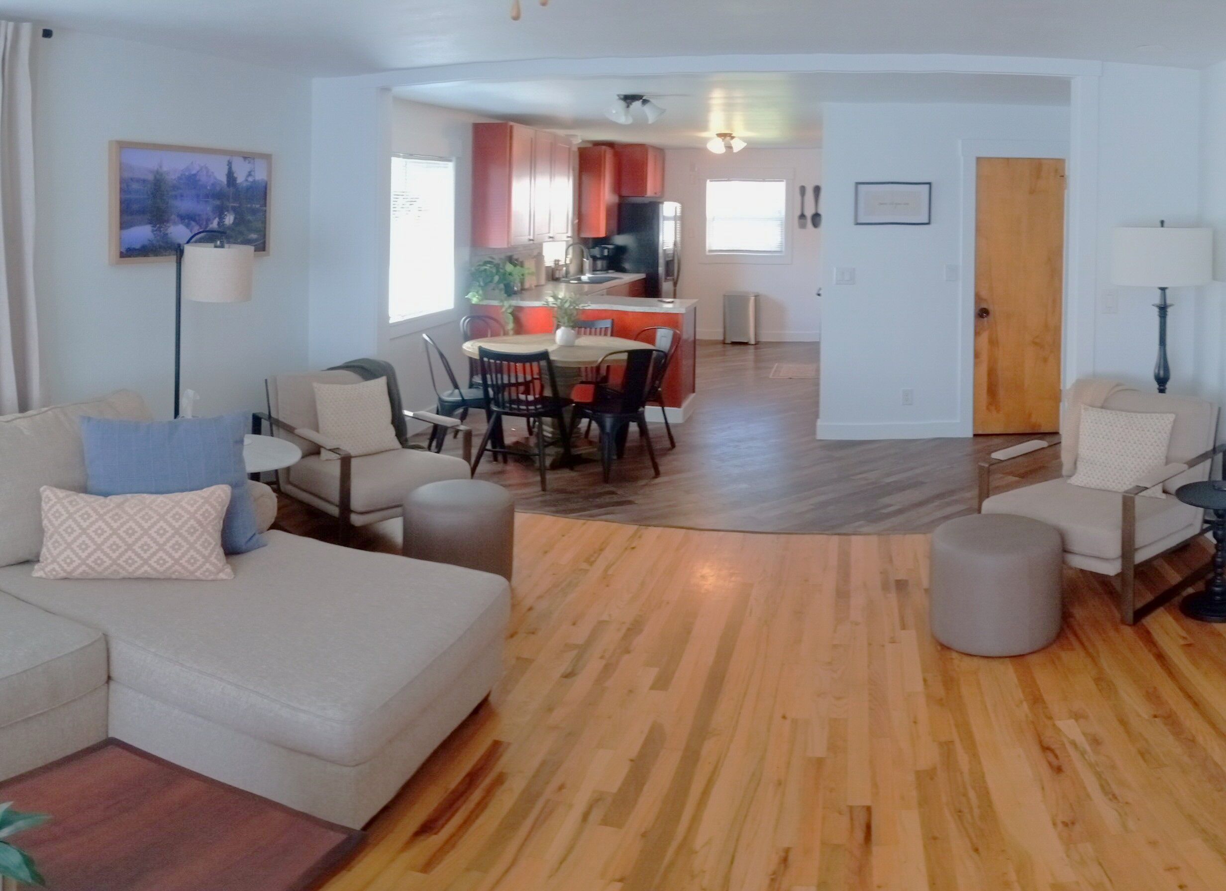 A living room with a sofa, chairs, a dining table, and a kitchen area in the background.