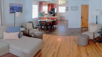 A living room with a sofa, chairs, a dining table, and a kitchen area in the background.